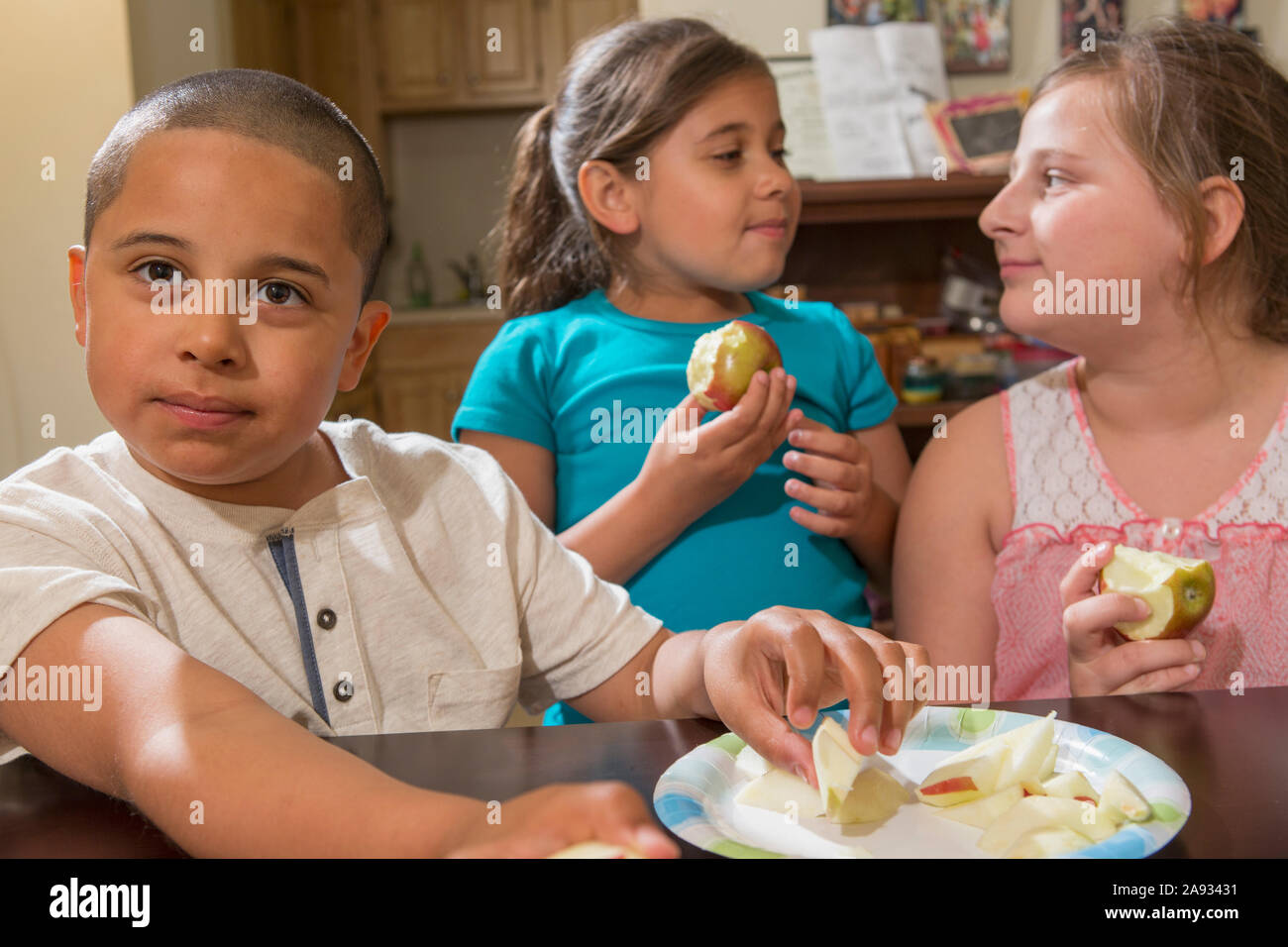 Hispanic boy with Autism eating apple with his sisters at home Stock Photo