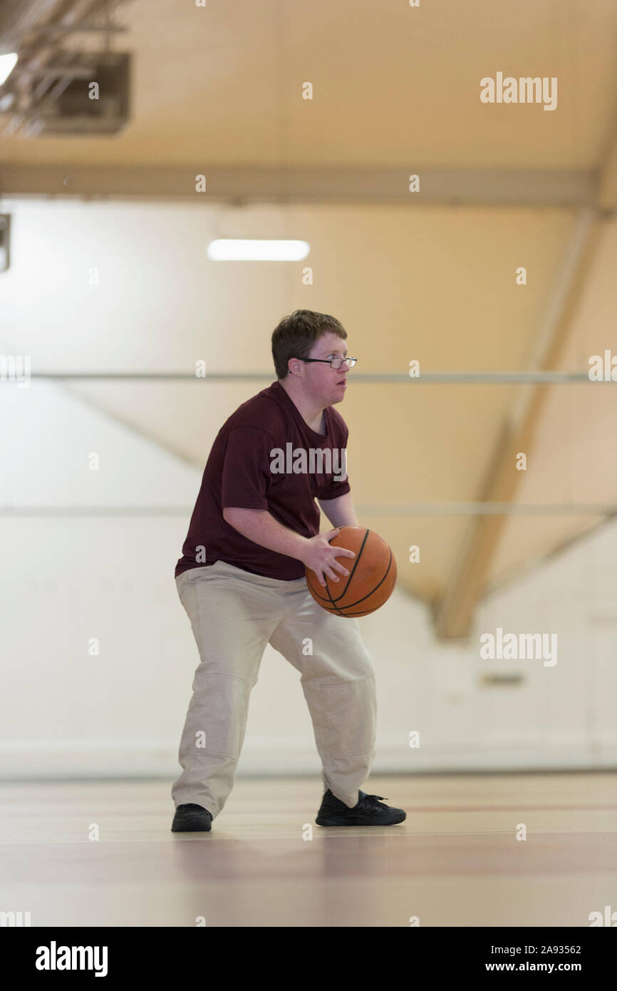 Young man with Down Syndrome playing basketball in school gym Stock
