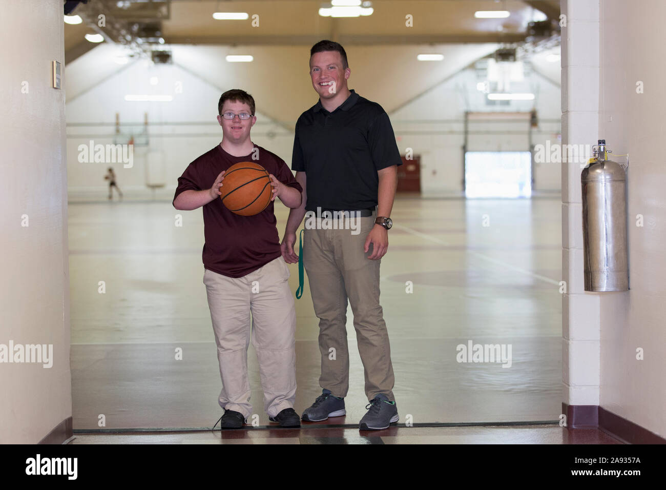 Young man with Down Syndrome playing basketball in school gym with his