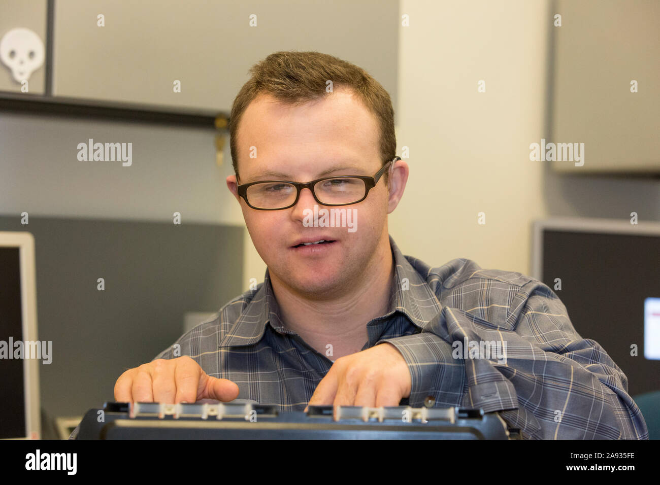 Happy hospital aid worker with Down Syndrome filing paperwork in office Stock Photo