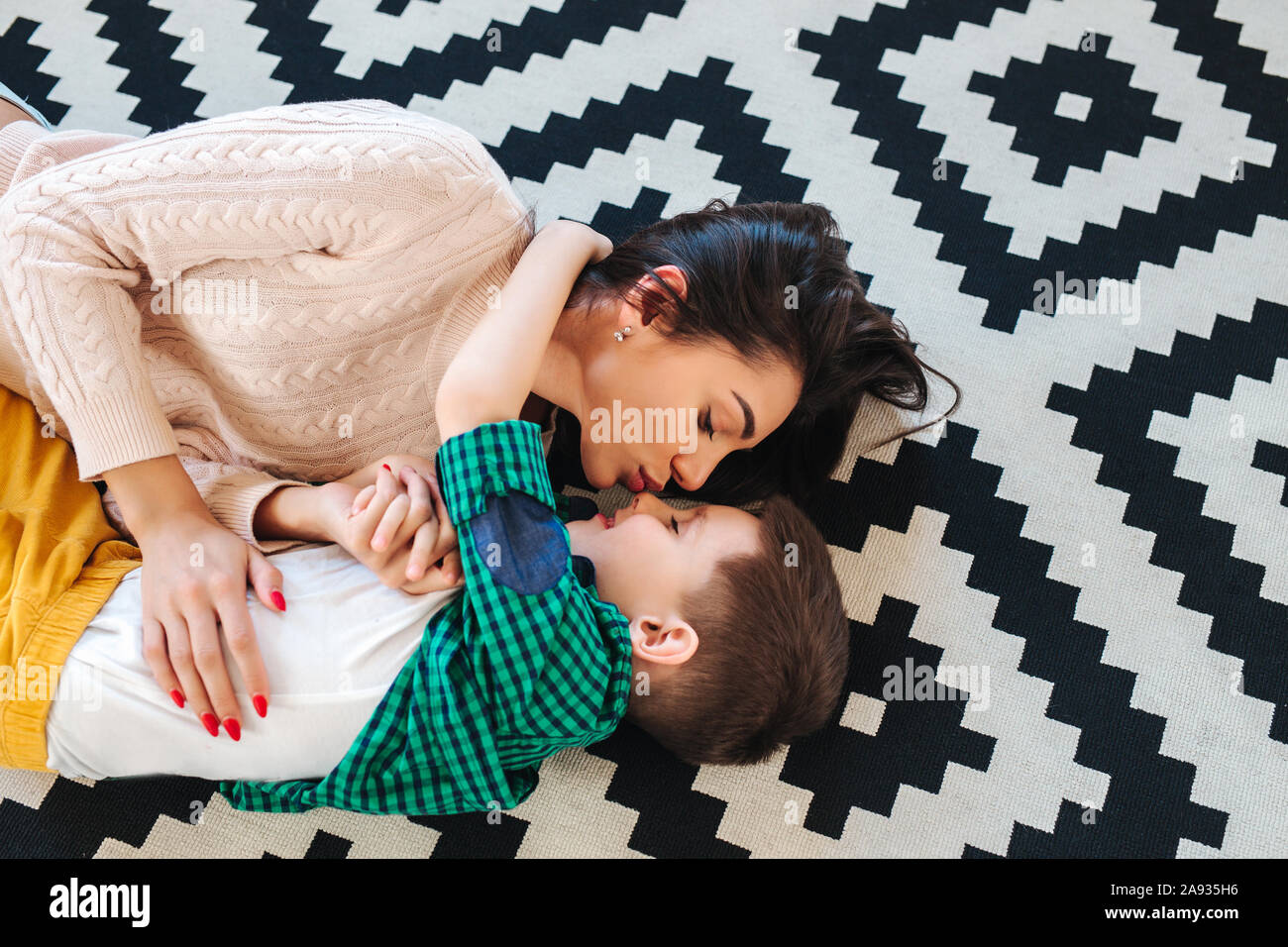 Young mother and her little son hugging , looking at each other and lying on floor Stock Photo