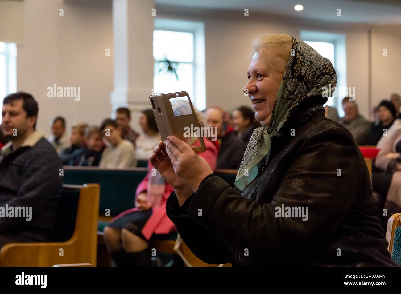 KOROSTEN - NOV, 10, 2019: An elderly woman in a scarf smiles and takes off a concert on the phone Stock Photo