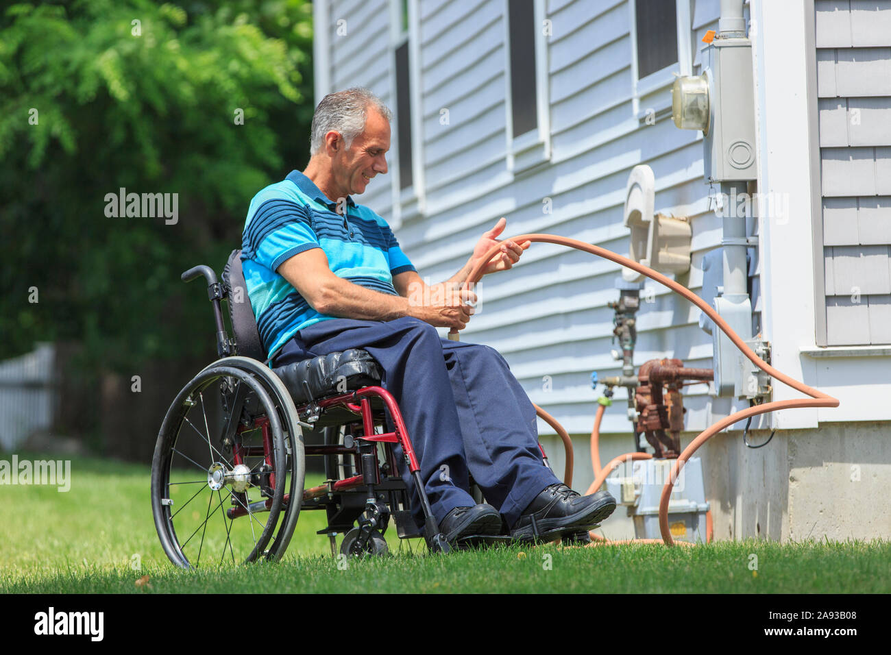 Man with Spinal Cord Injury in wheelchair arranging the hose on his house backyard Stock Photo