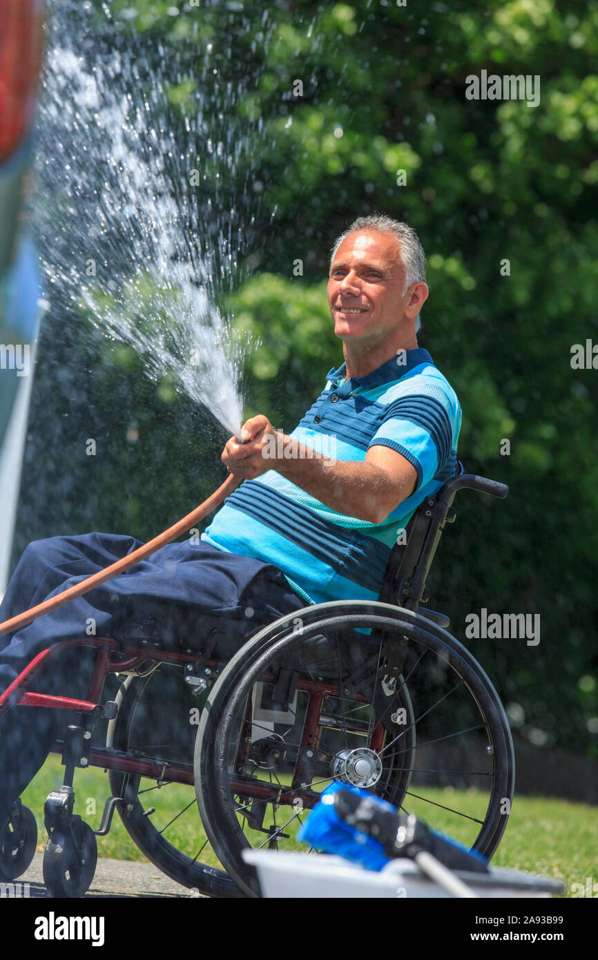 Man with a Spinal Cord Injury in wheelchair washing his accessible car Stock Photo
