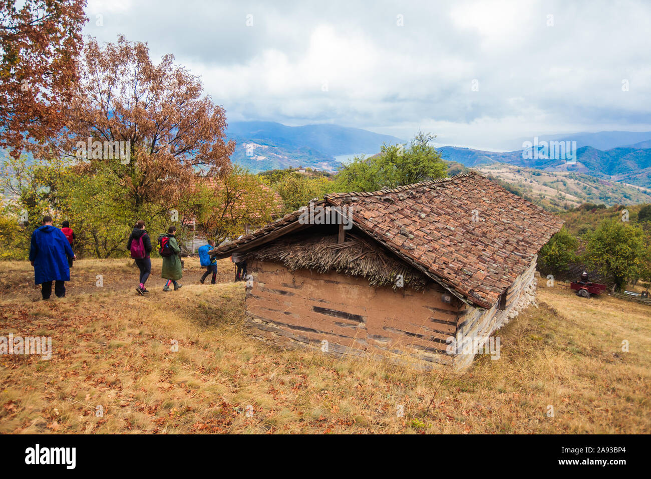 Group of active people hiking on the rainy autumn day wearing a raincoat. Real unrecognizable hikers, rearview, cloudy sky in the background. Stock Photo