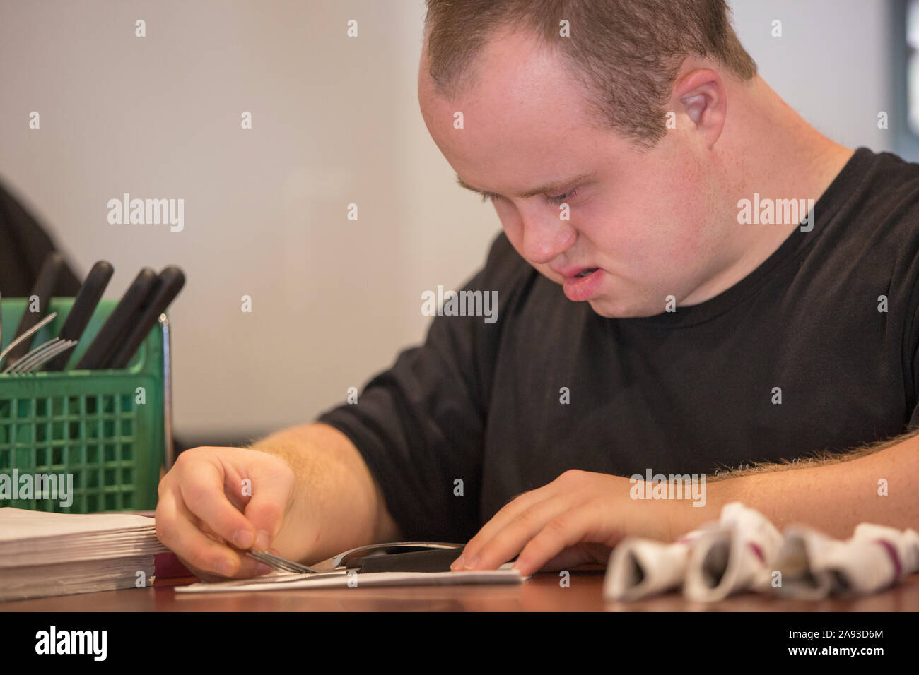 Waiter with Down Syndrome preparing napkin and silver in a restaurant Stock Photo