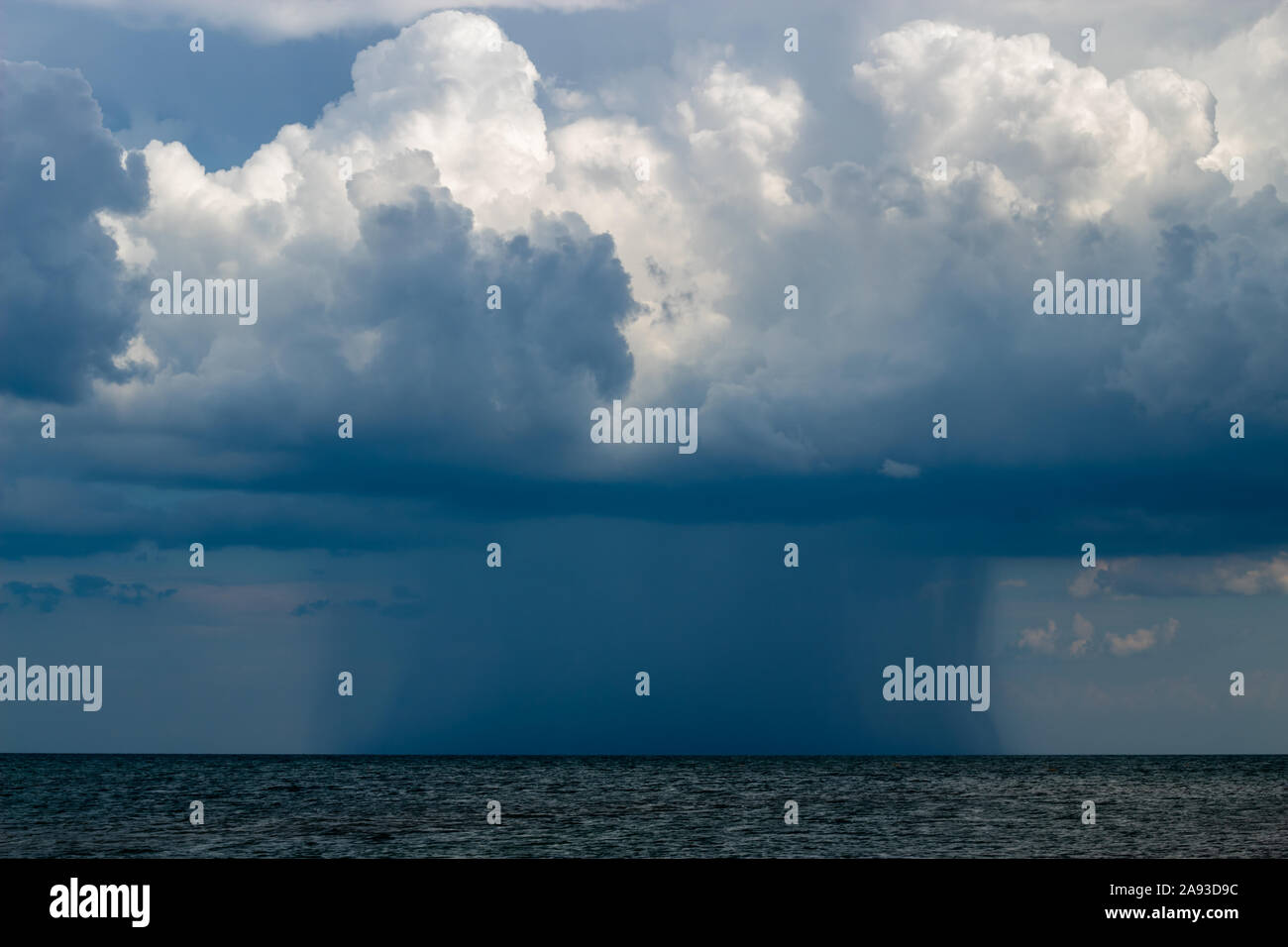 Thunderstorm on the horizon in the sea. Gray thunderclouds. In the distance, the size of the elements is clearly visible. Stock Photo
