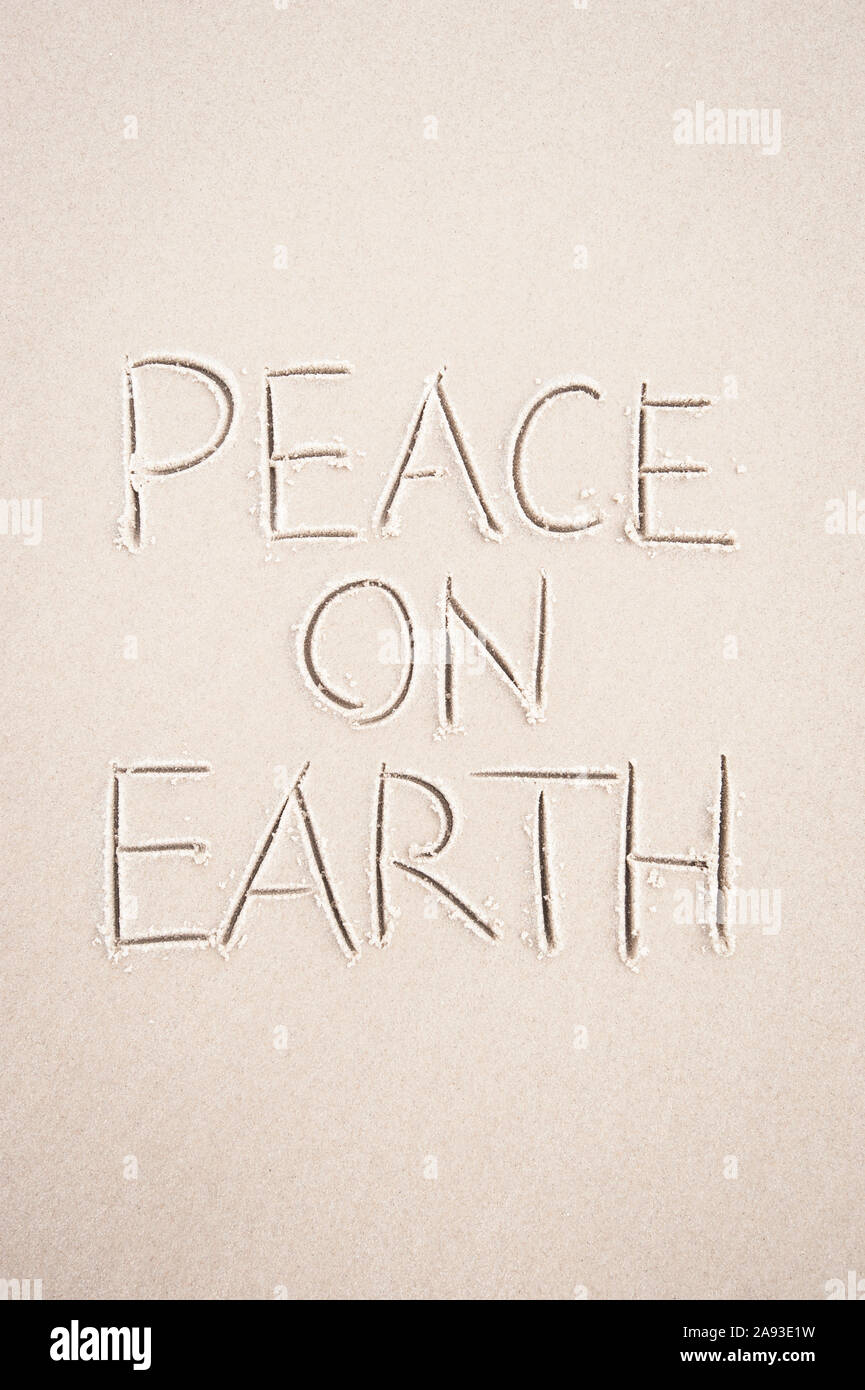 Peace On Earth holiday message handwritten on smooth sand beach Stock Photo