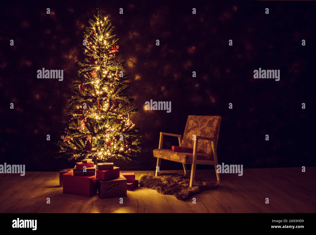 Decorated magical Christmas tree in front of black wall with Christmas red paper wrapped presents under the tree, retro chair next to it. Night. Stock Photo