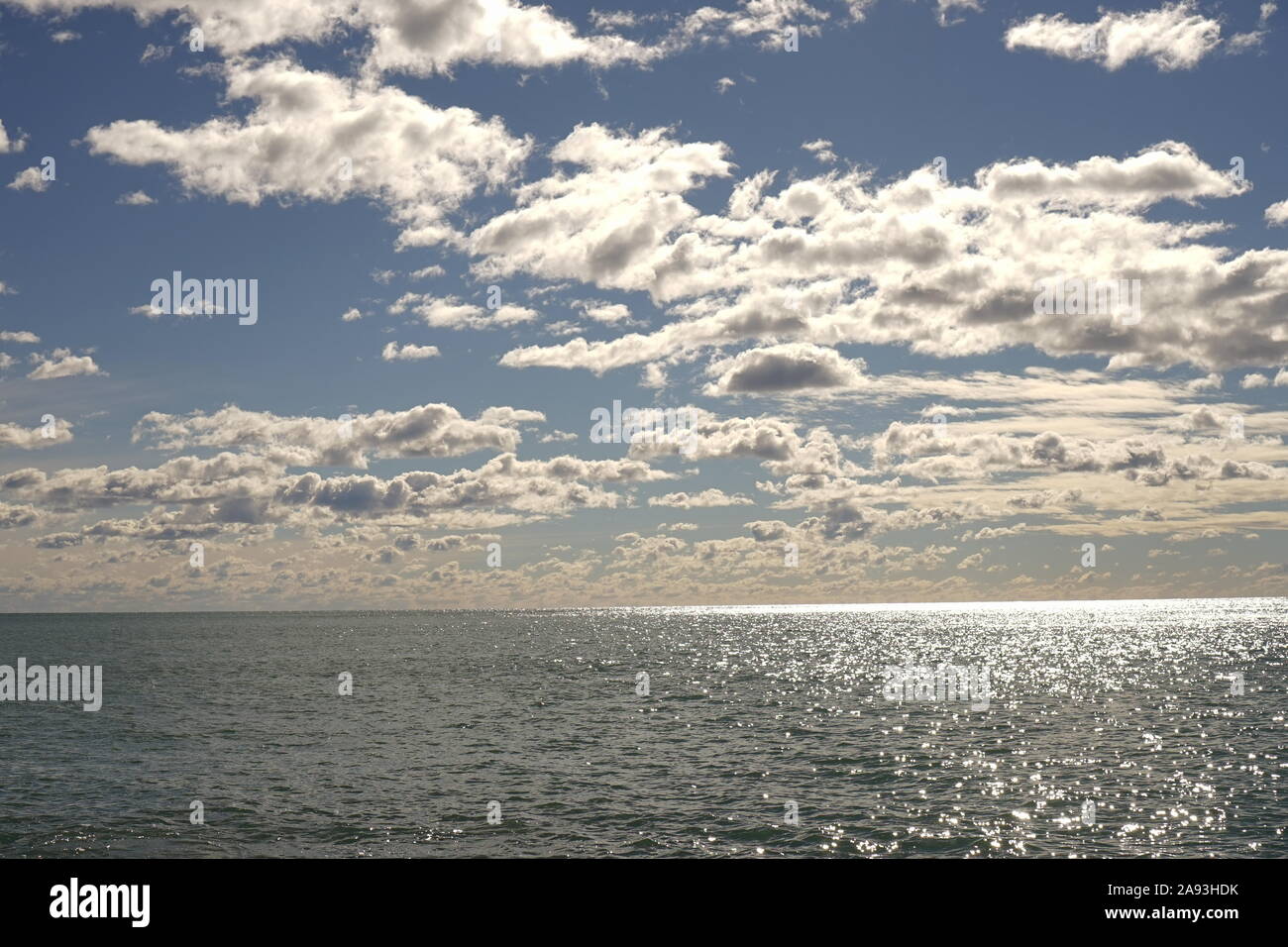 White fluffy clouds over the sun lit ocean Stock Photo