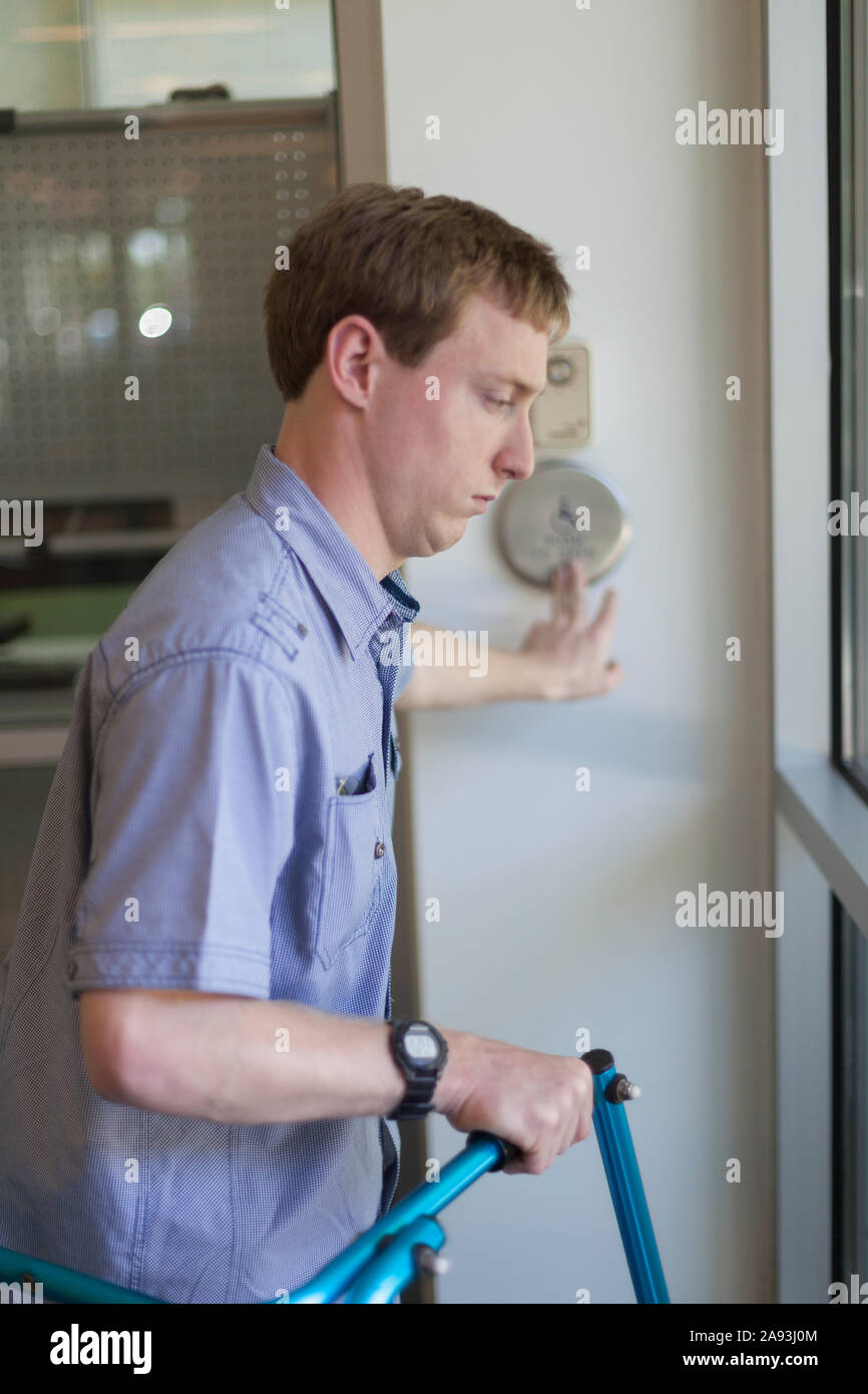 Young man with Cerebral Palsy using his walker while opening a door with a push button Stock Photo