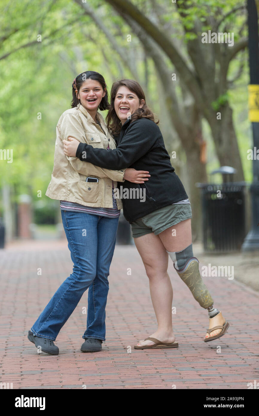 Two happy young female friends hugging, one with a prosthetic leg Stock Photo