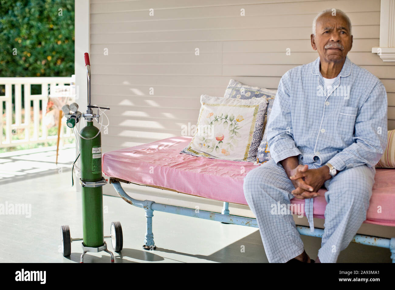 Elderly man sitting on the deck of rest-home next to oxygen bottle. Stock Photo