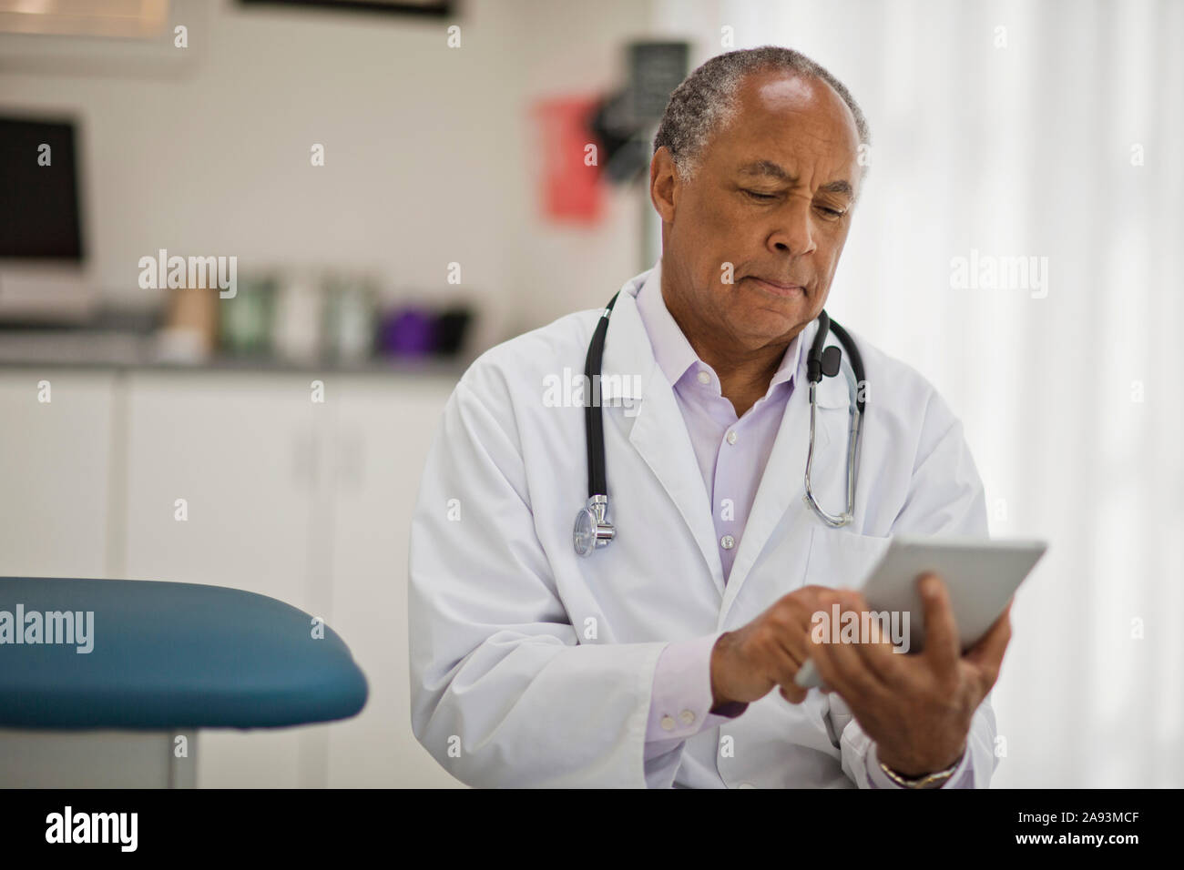 Contemplative male doctor using a digital tablet while sitting inside his office. Stock Photo