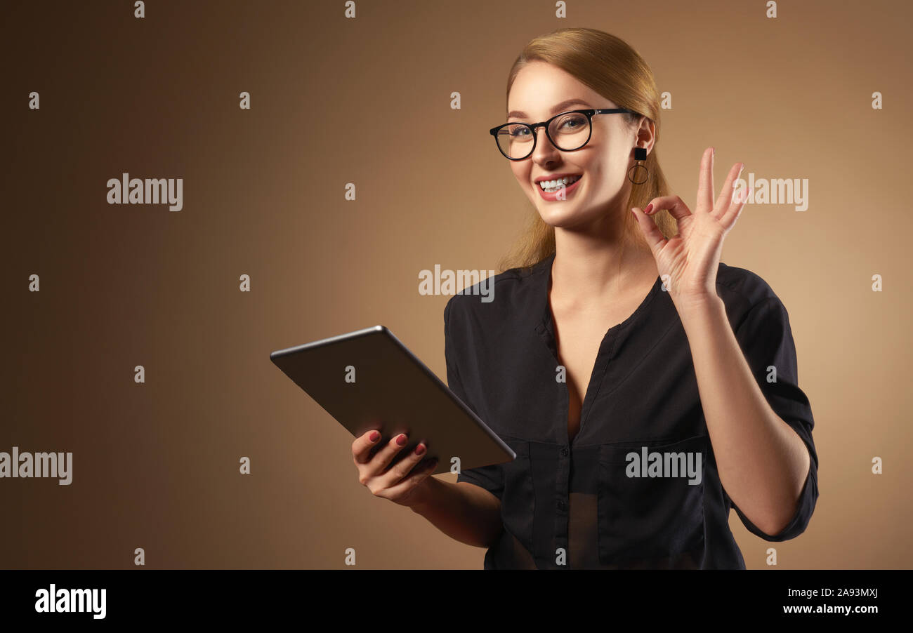 Happy professional girl wearing glasses and holding tablet on brown background Stock Photo