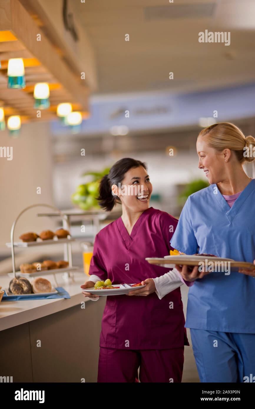 Two young nurses smile and chat together as they get their lunch from the hospital canteen Stock Photo