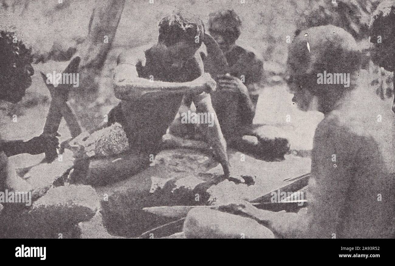 Australian Aborigines performing ritual of pouring blood from arm vein into a hole sacred to wallabies to ensure food source remains good 1930s. Stock Photo