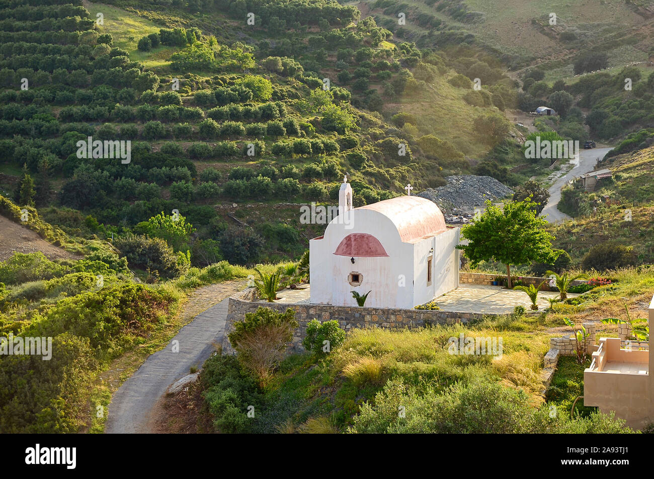 Idyllic rural landscape with hills covered by olive trees and tiny peaceful orthodox church in beautiful sunset light, Crete, Greece. Stock Photo