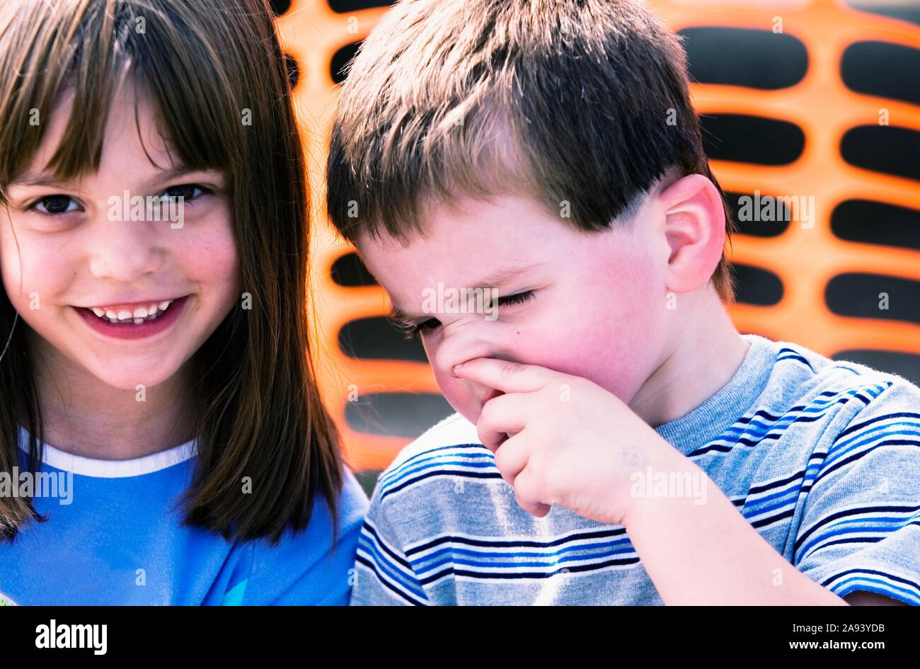 Little boy picking his nose while his sister looks on with a smile Stock Photo