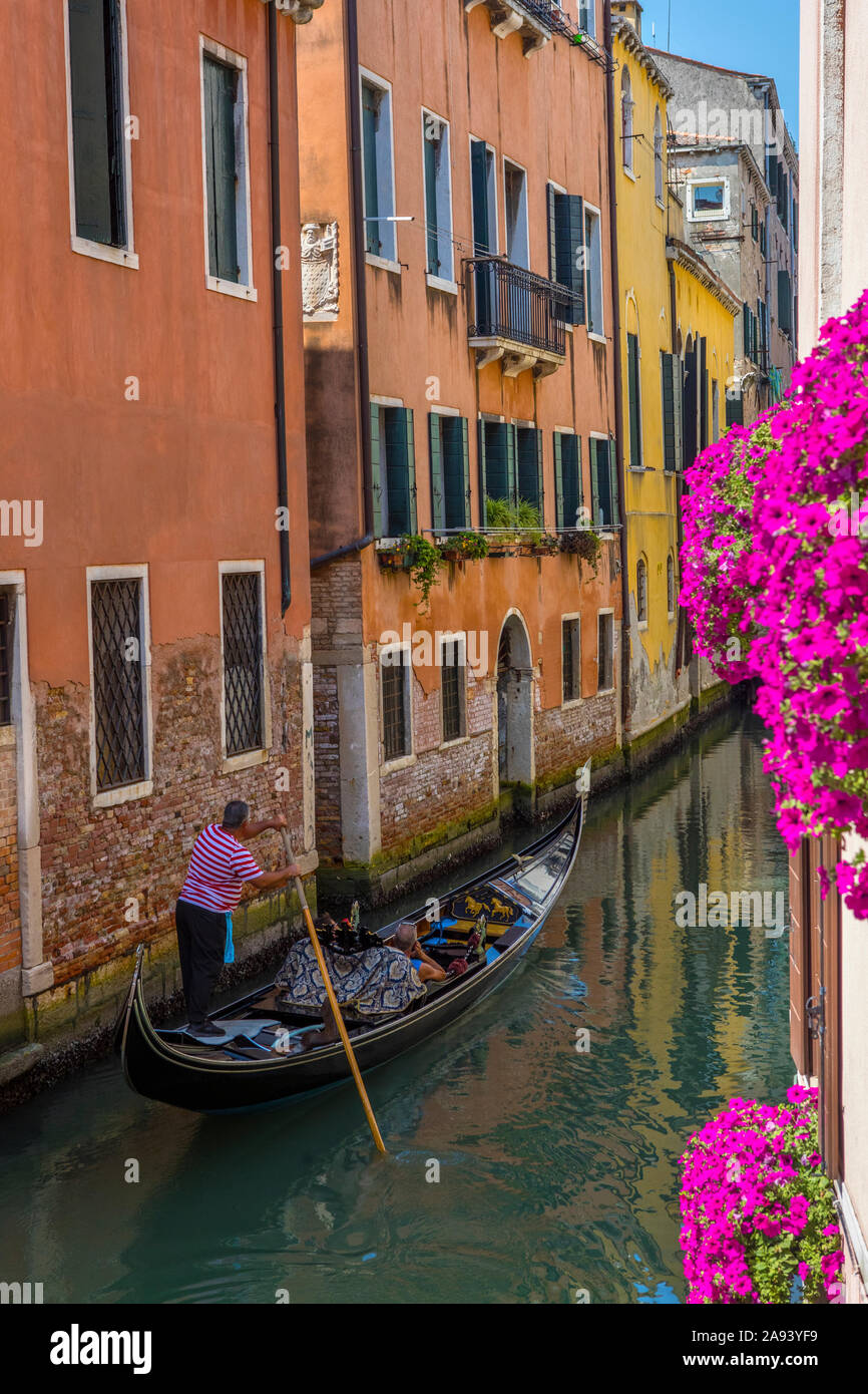 Venice, Italy - July 20th 2019: A couple enjoying a romantic Gondola ride through the narrow canalways of the historic city of Venice in Italy. Stock Photo