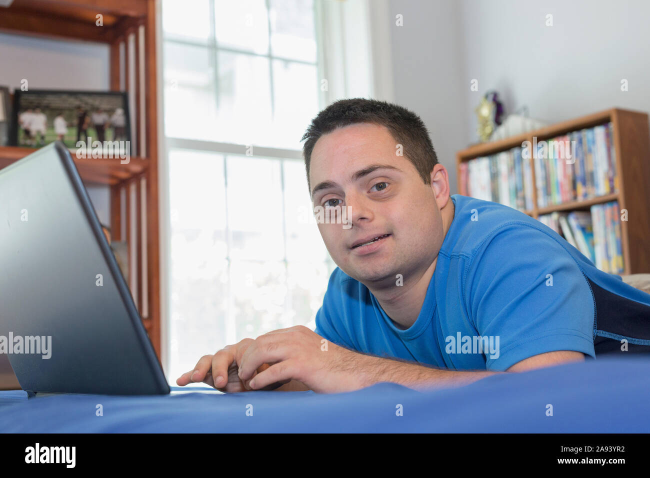 Man with Down Syndrome lying on bed using a laptop Stock Photo