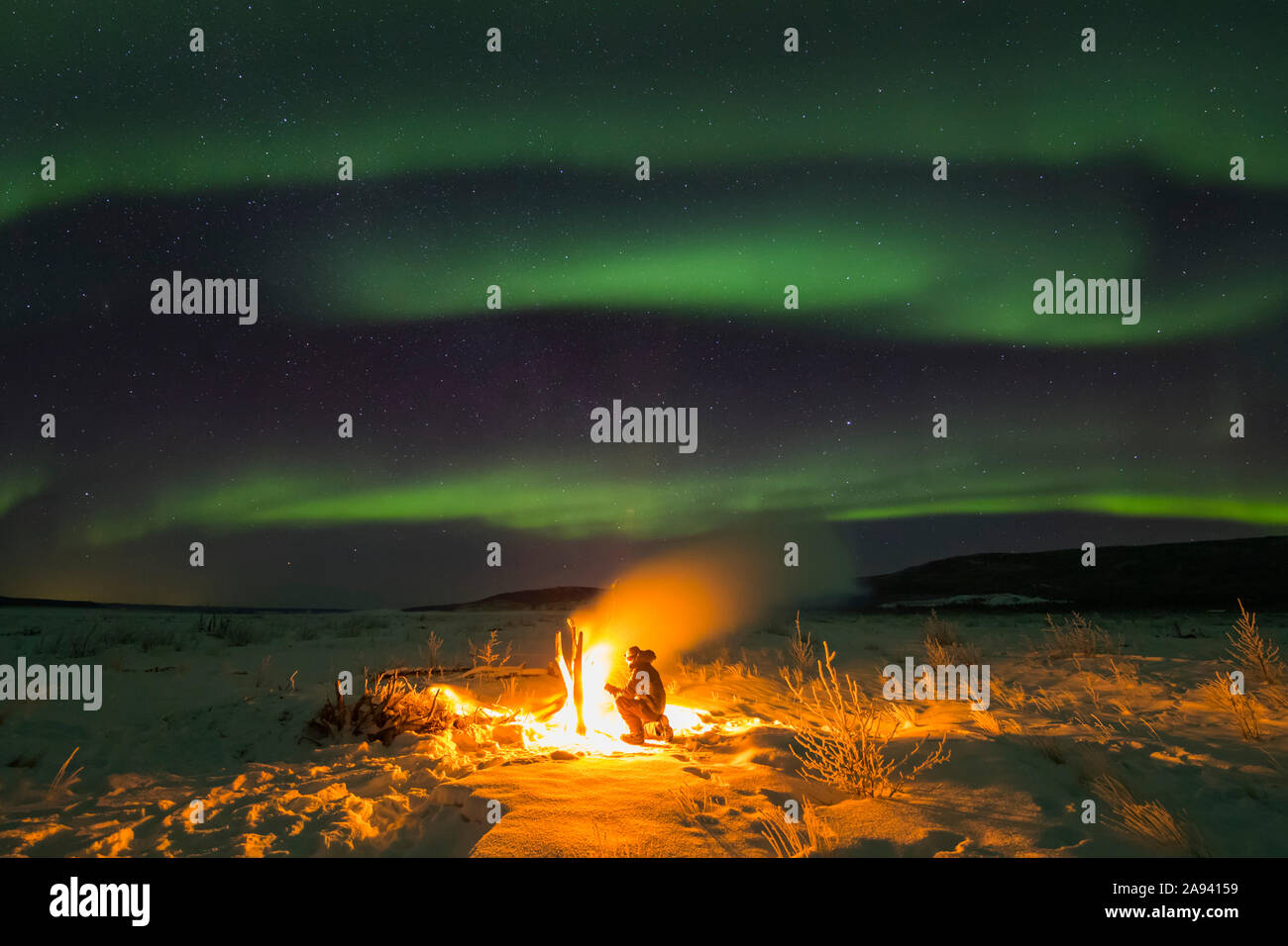 Staying warm beside a campfire on the Delta River while watching the aurora borealis on a frigid night; Alaska, United States of America Stock Photo