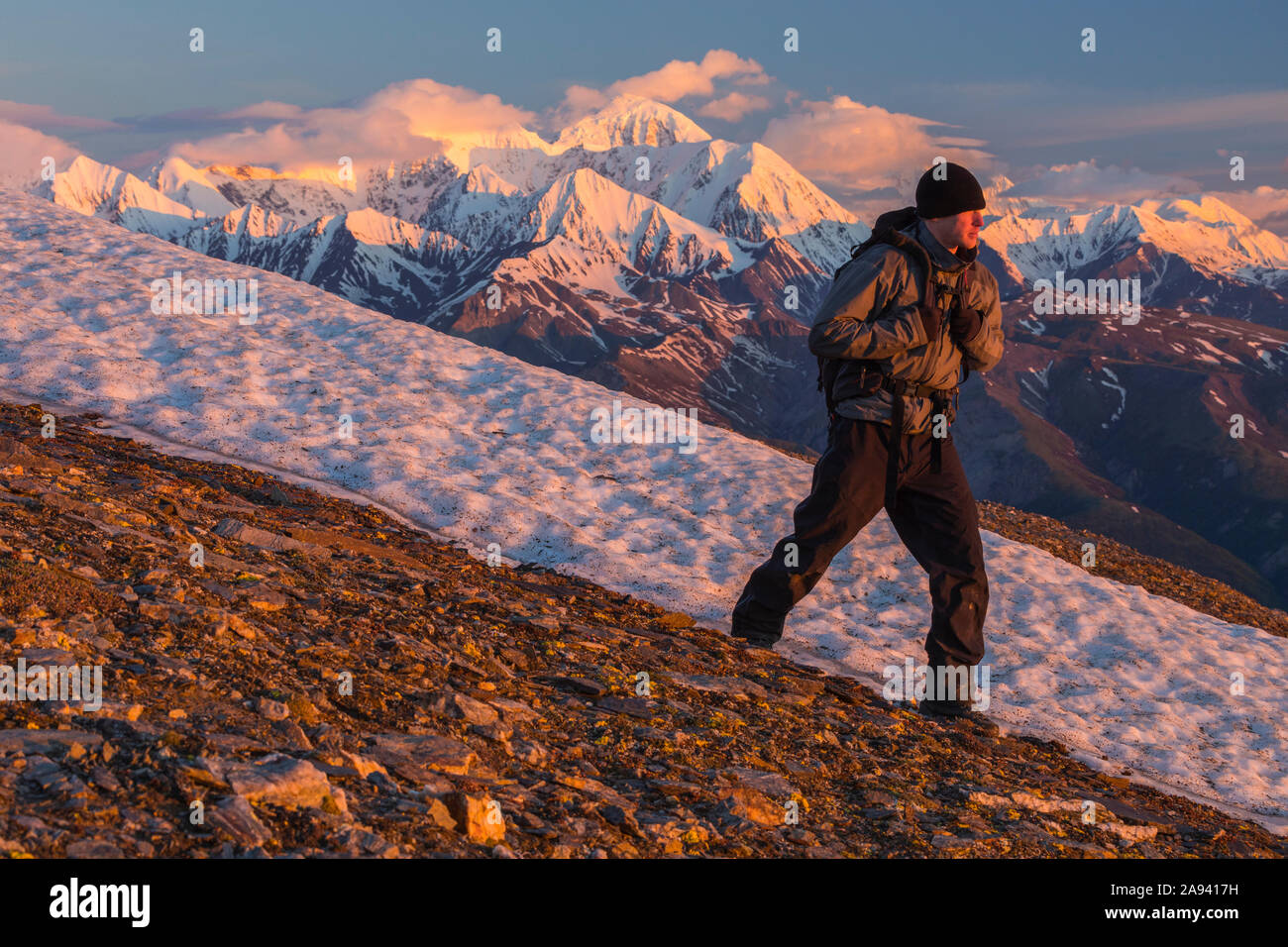 A hiker traverses a mountain slope in the Alaska Range at sunrise; Alaska, United States of America Stock Photo