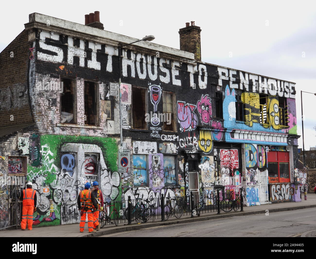 Builders in front of a decrepit building occupied by squatters and covered in graffiti protesting against gentrification. Hackney Wick, East London. Stock Photo