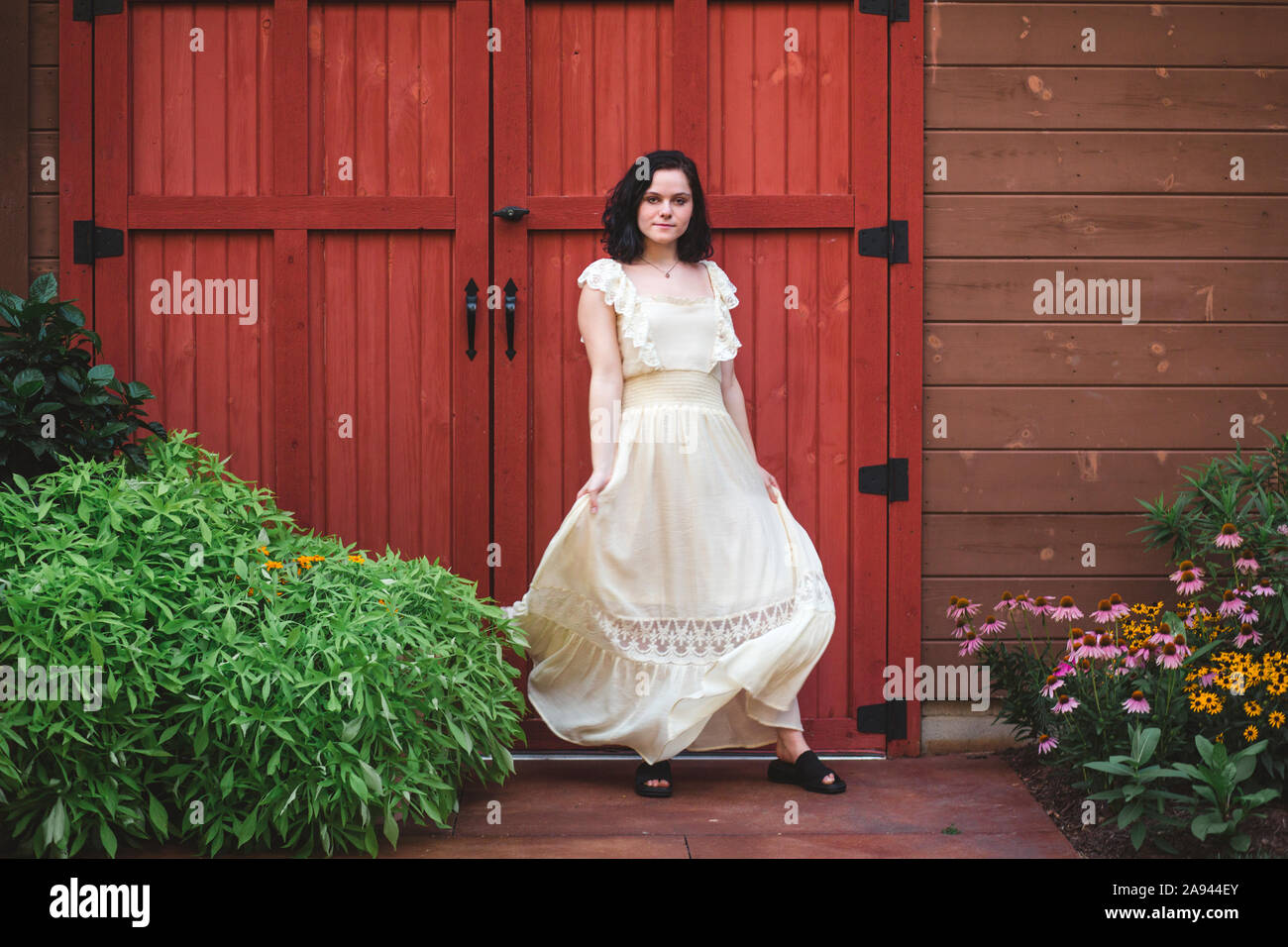 A young woman stands in a flower garden in front of large wooden door Stock Photo