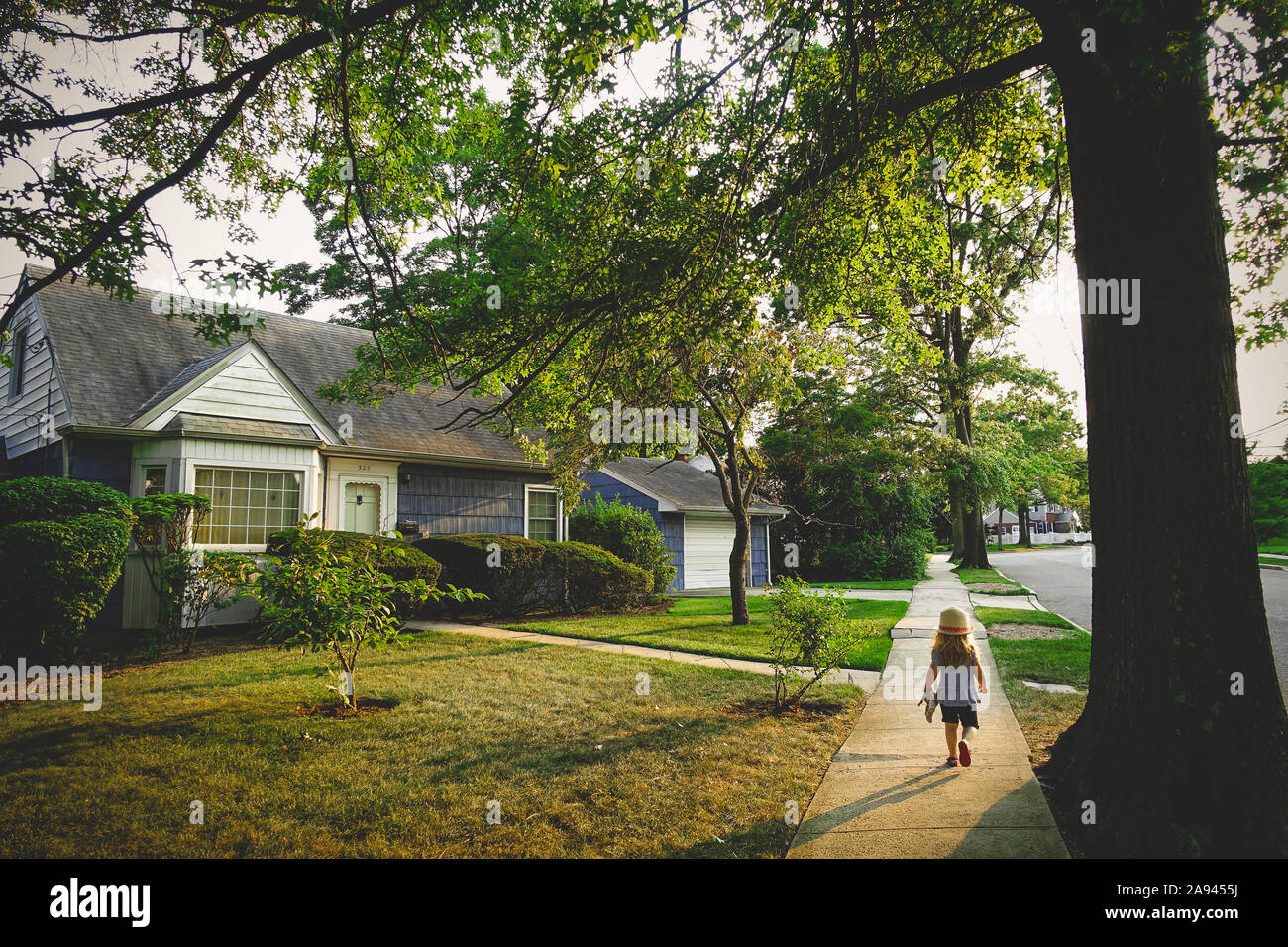 A little girl walks on a pathway by a blue house. Stock Photo