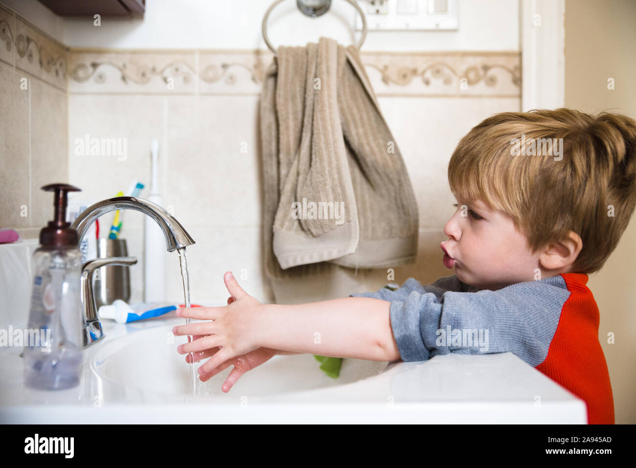 A little boy washes his hands in the bathroom sink. Stock Photo