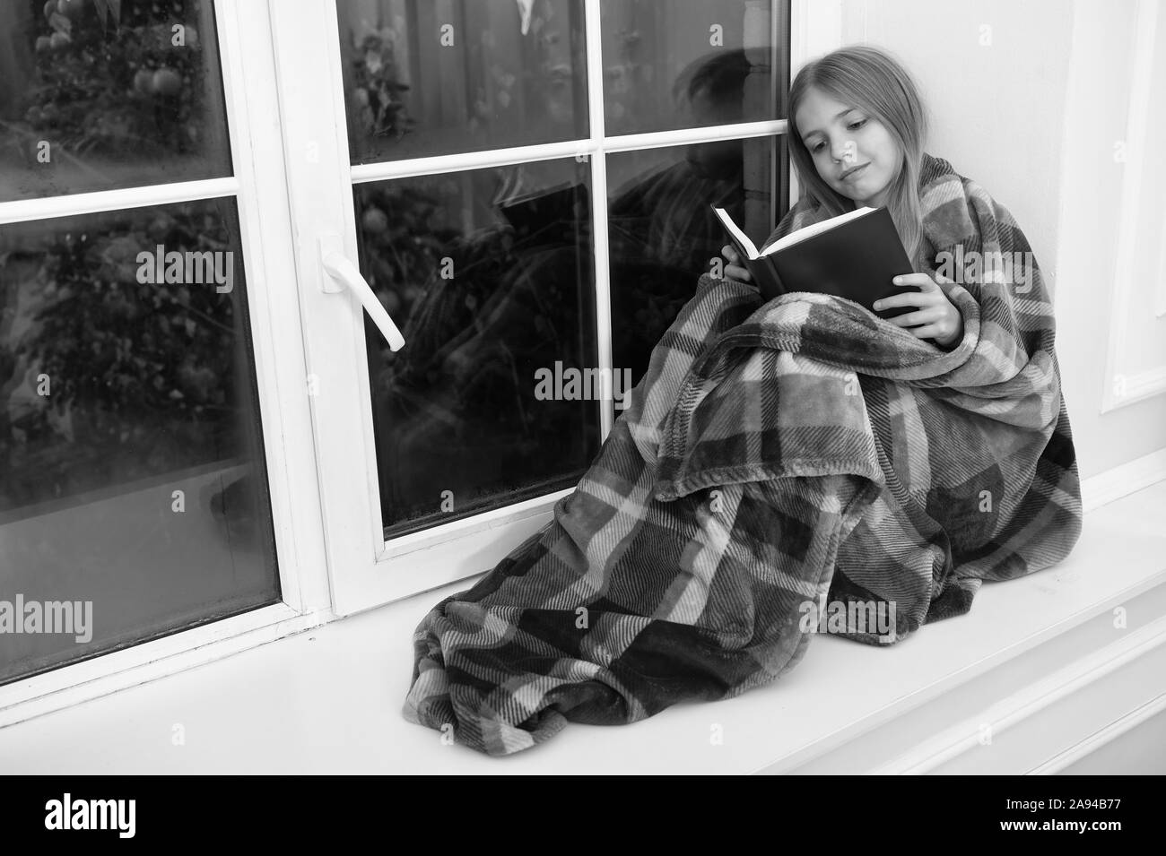 Merry Christmas. Little girl enjoy reading Christmas story. Little child read book on Christmas eve. Little reader wrapped in plaid sit on window sill. Childrens picture book. Magic xmas spirit. Stock Photo