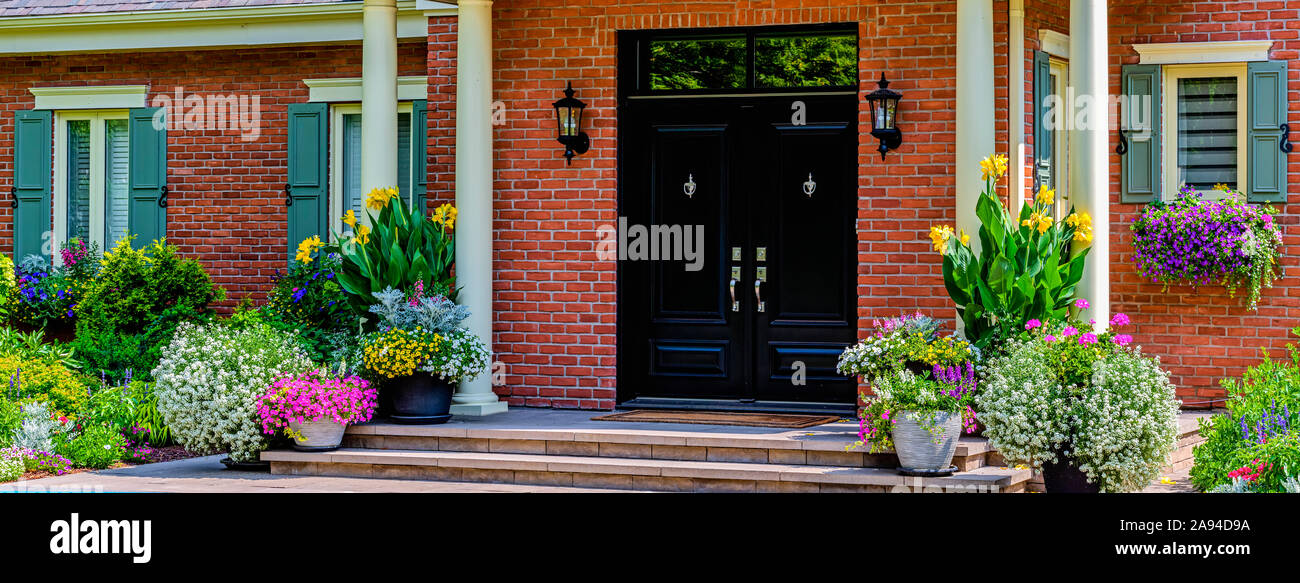 Double doors at the entrance of a stately home with blossoming flowers decorating the front; Hudson, Quebec, Canada Stock Photo