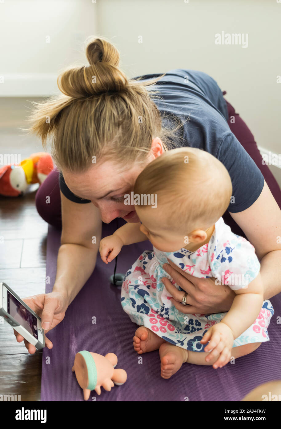 Mother showing image on smart phone to baby daughter; Vancouver, British Columbia, Canada Stock Photo