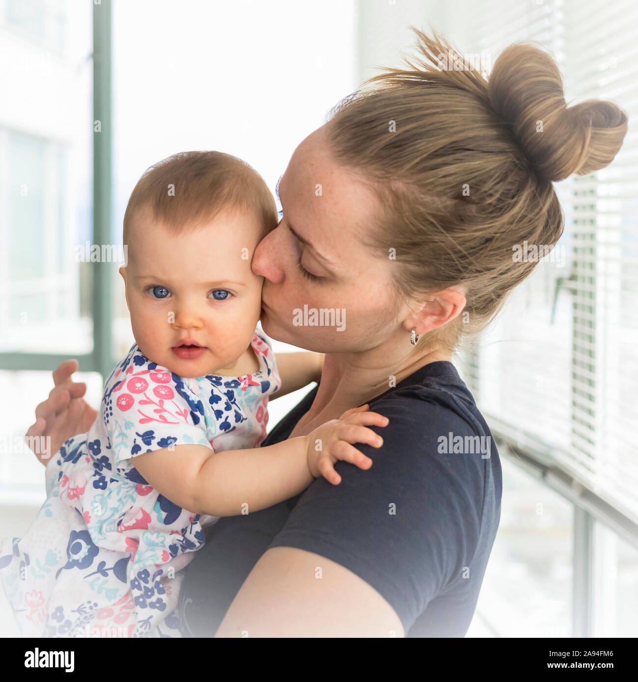Portrait of infant baby girl with mother at home, mother kissing baby on the cheek; Vancouver, British Columbia, Canada Stock Photo