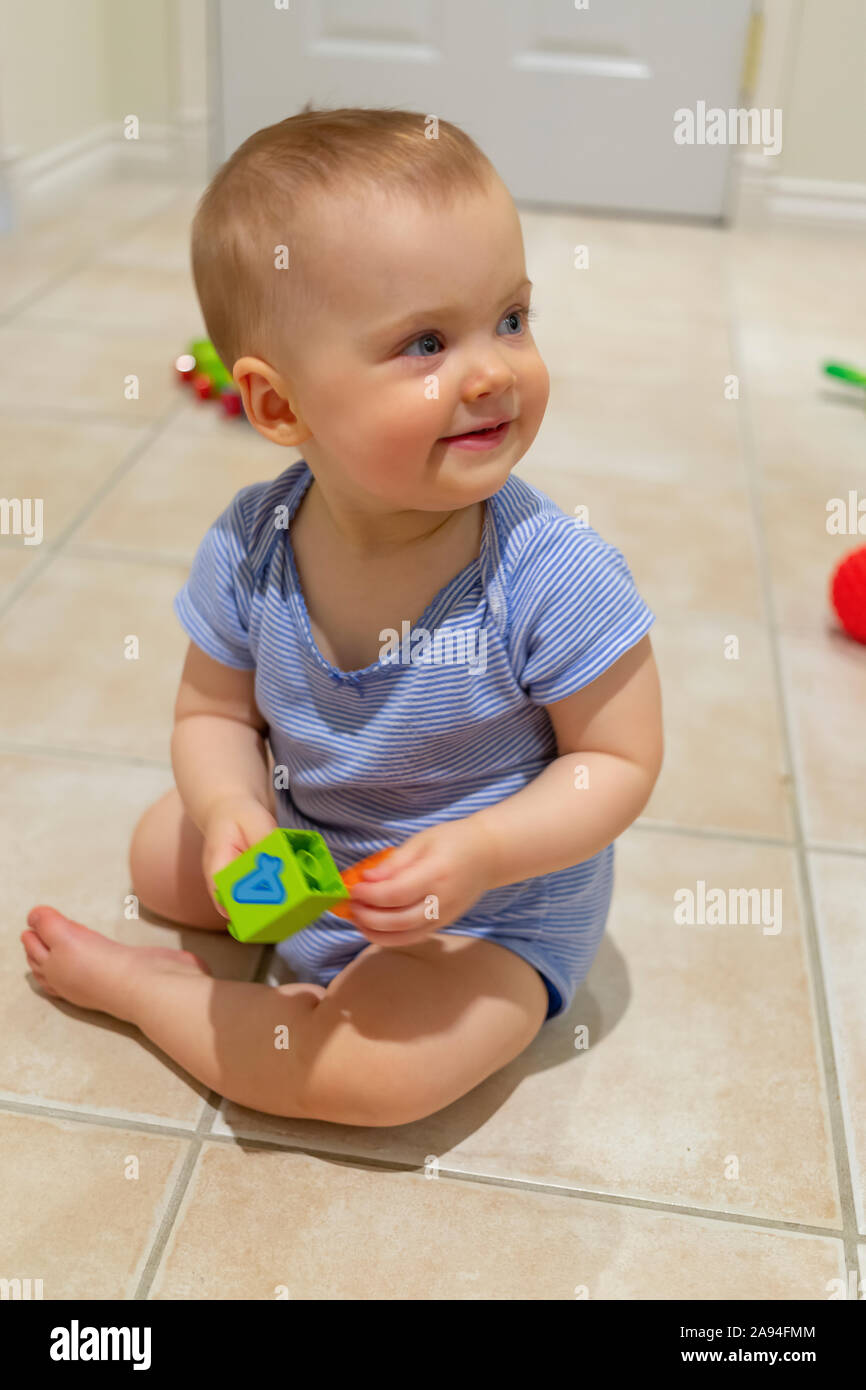 A baby girl sits on the floor at home playing with a toy; Vancouver, British Columbia, Canada Stock Photo