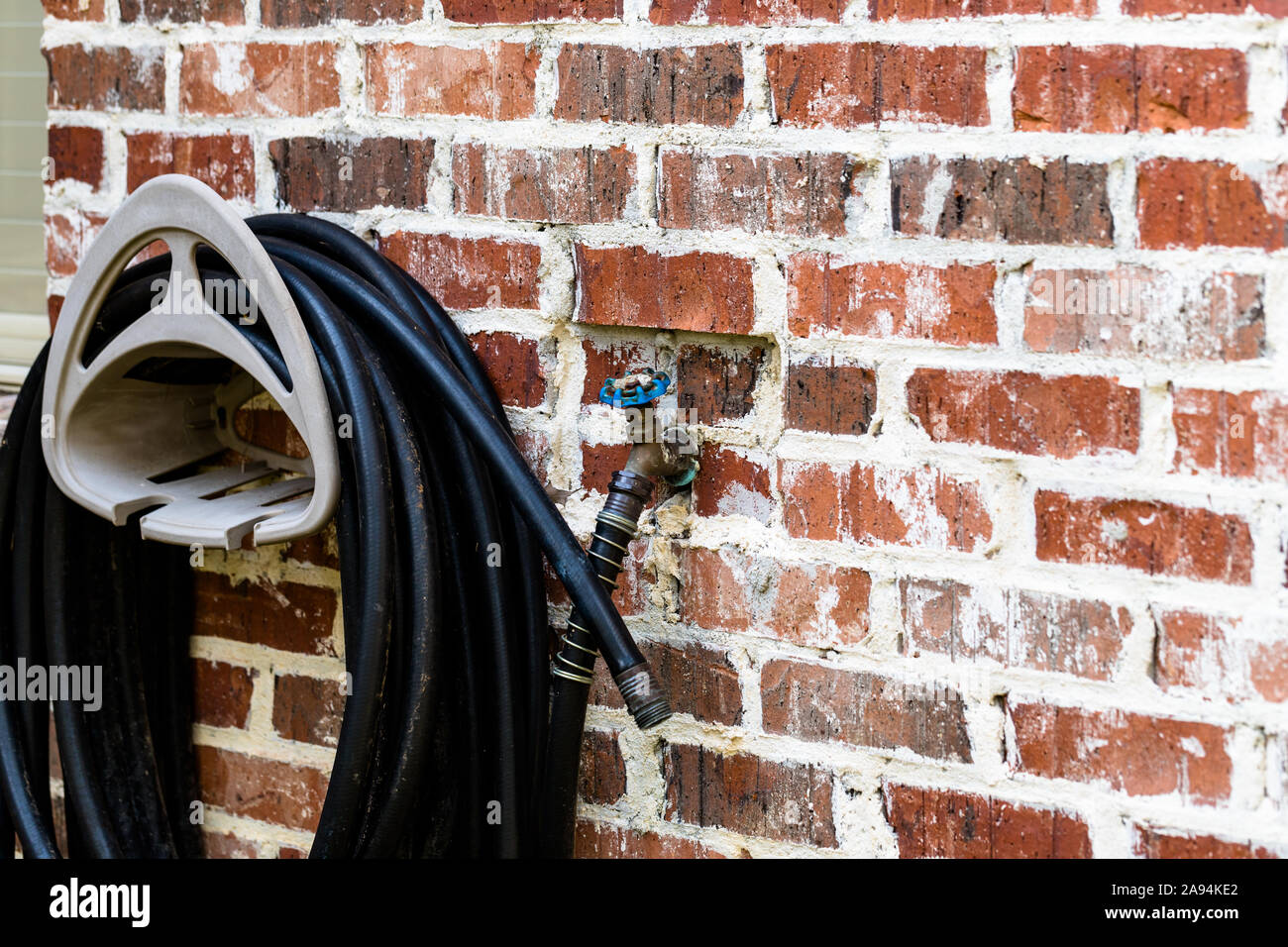 Rubber garden hose hanging on brick wall of house. Stock Photo