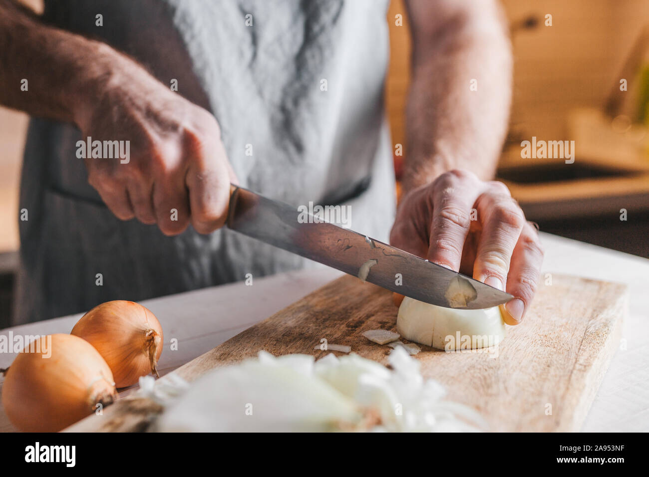 Rude male hands cut a white onion with a knife on the background of the kitchen Stock Photo