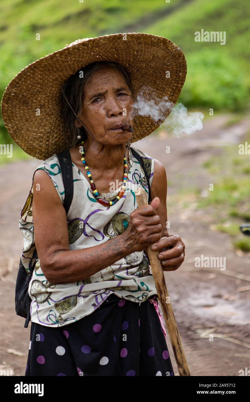 A woman smoking a hand made cigarette whilst walking with a stick near