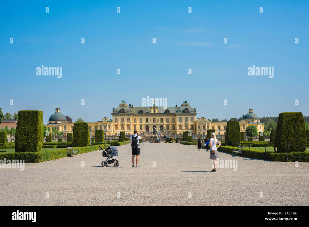Young family holiday, view in summer of young parents standing in the Baroque garden at Drottningholm and looking back at the palace building, Sweden. Stock Photo