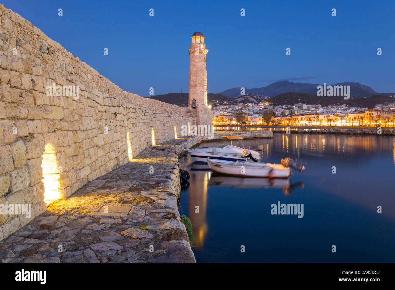 Rethymno, Crete, Greece. View along wall of the Venetian Harbour to illuminated 16th century Turkish lighthouse, dusk. Stock Photo