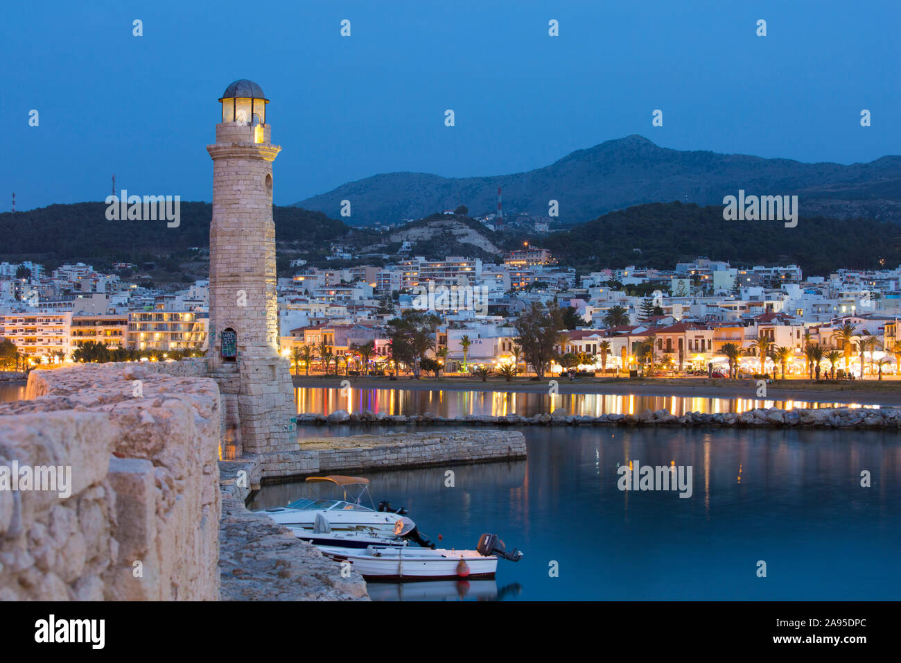 Rethymno, Crete, Greece. View along wall of the Venetian Harbour to illuminated 16th century Turkish lighthouse, dusk. Stock Photo