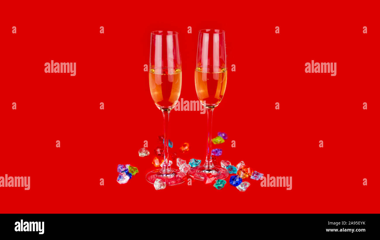 Glasses of champagne on red background and sparkling crystal stones on base ant foreground. New year or romantic celebration. Luxury. Free space Stock Photo
