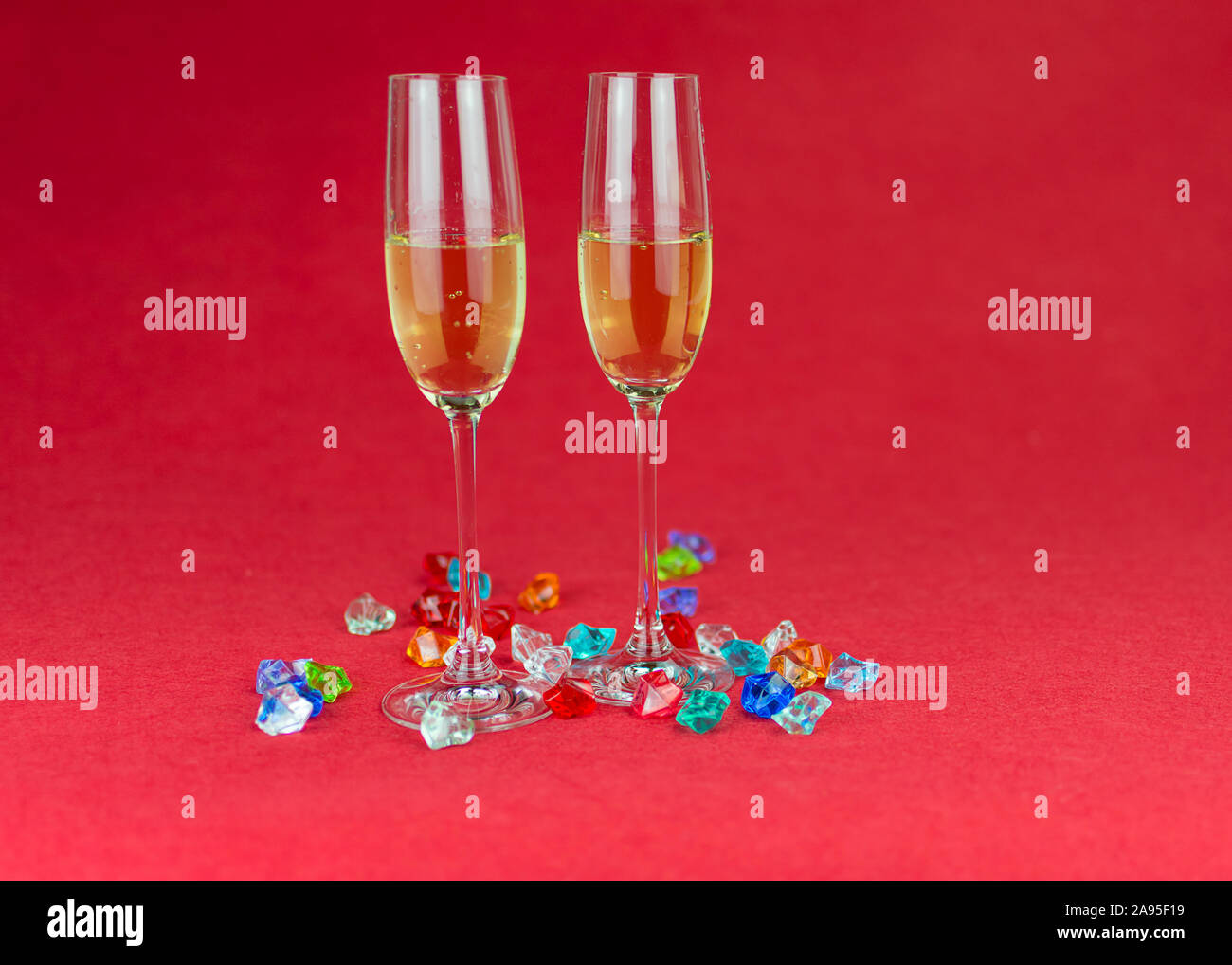 Glasses of champagne on red background and sparkling crystal stones on base ant foreground. New year or romantic celebration. Luxury. Free space Stock Photo