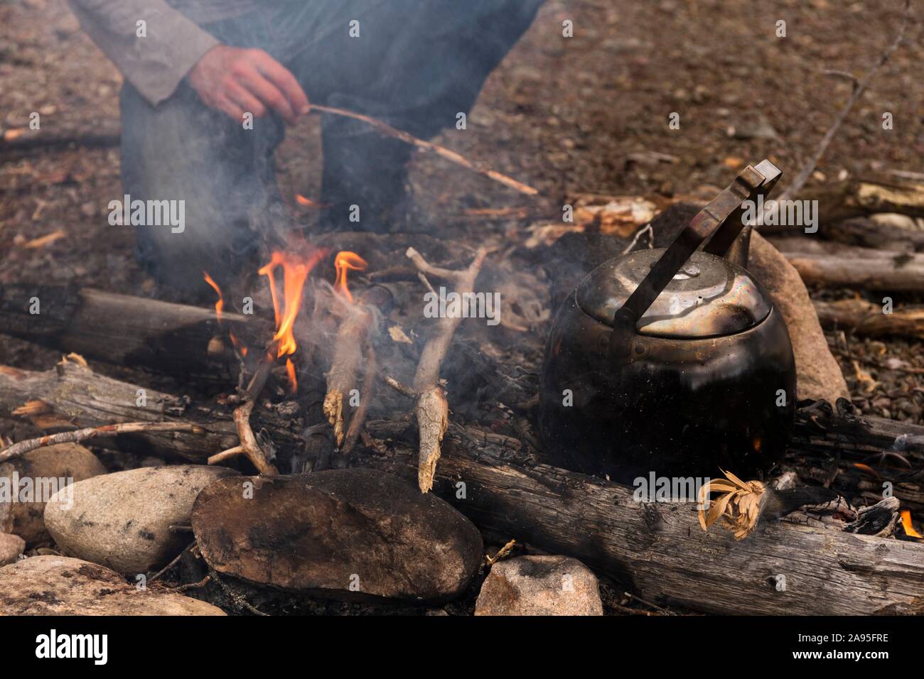 https://c8.alamy.com/comp/2A95FRE/coffee-kettle-on-the-campfire-behind-it-the-legs-of-a-person-kneeling-at-the-campfire-harjedalen-sweden-2A95FRE.jpg