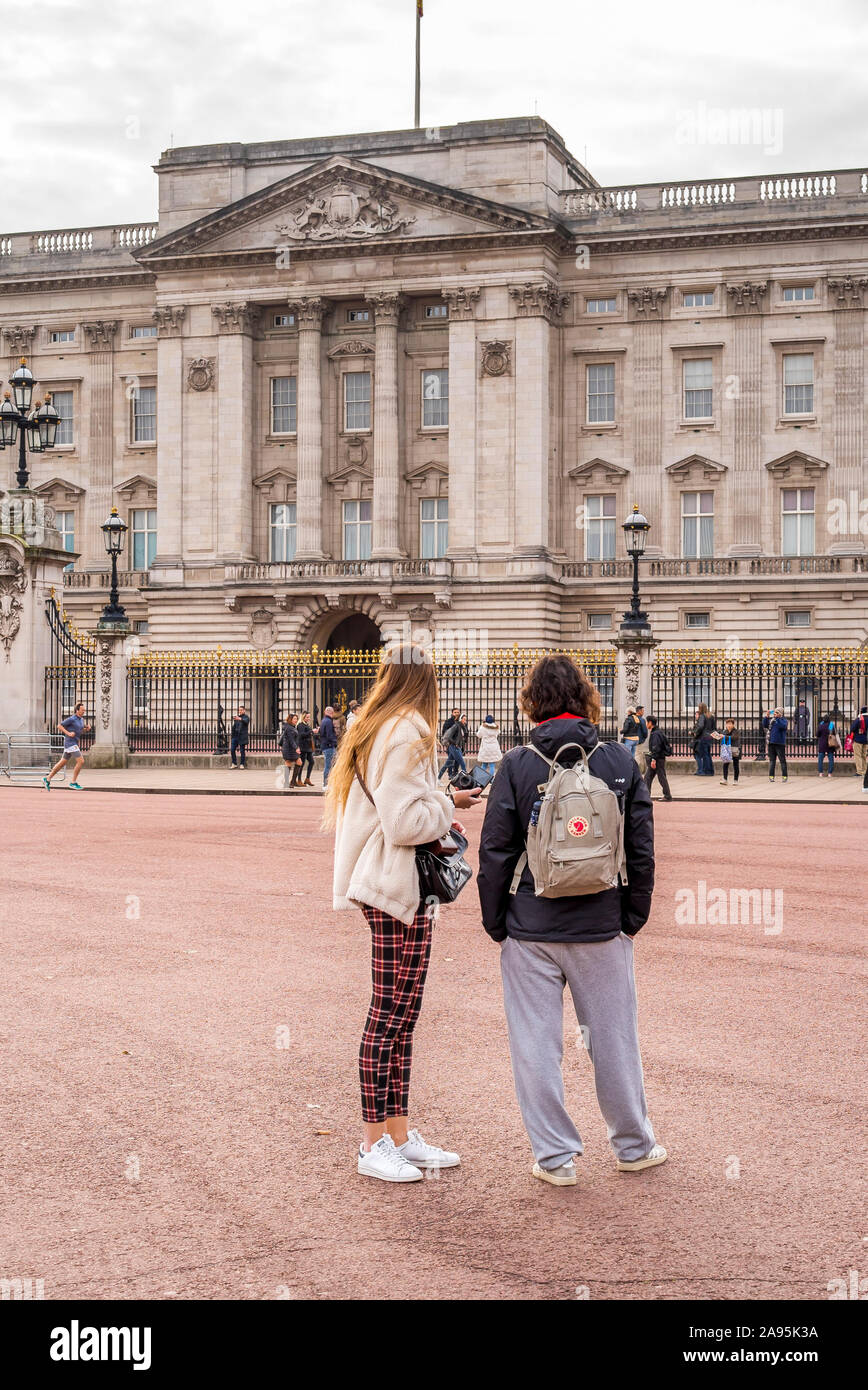 Tourists from behind, rear view, looking at her majesty's royal residence (famous London landmark) Buckingham Palace, City of Westminster, London, UK. Stock Photo