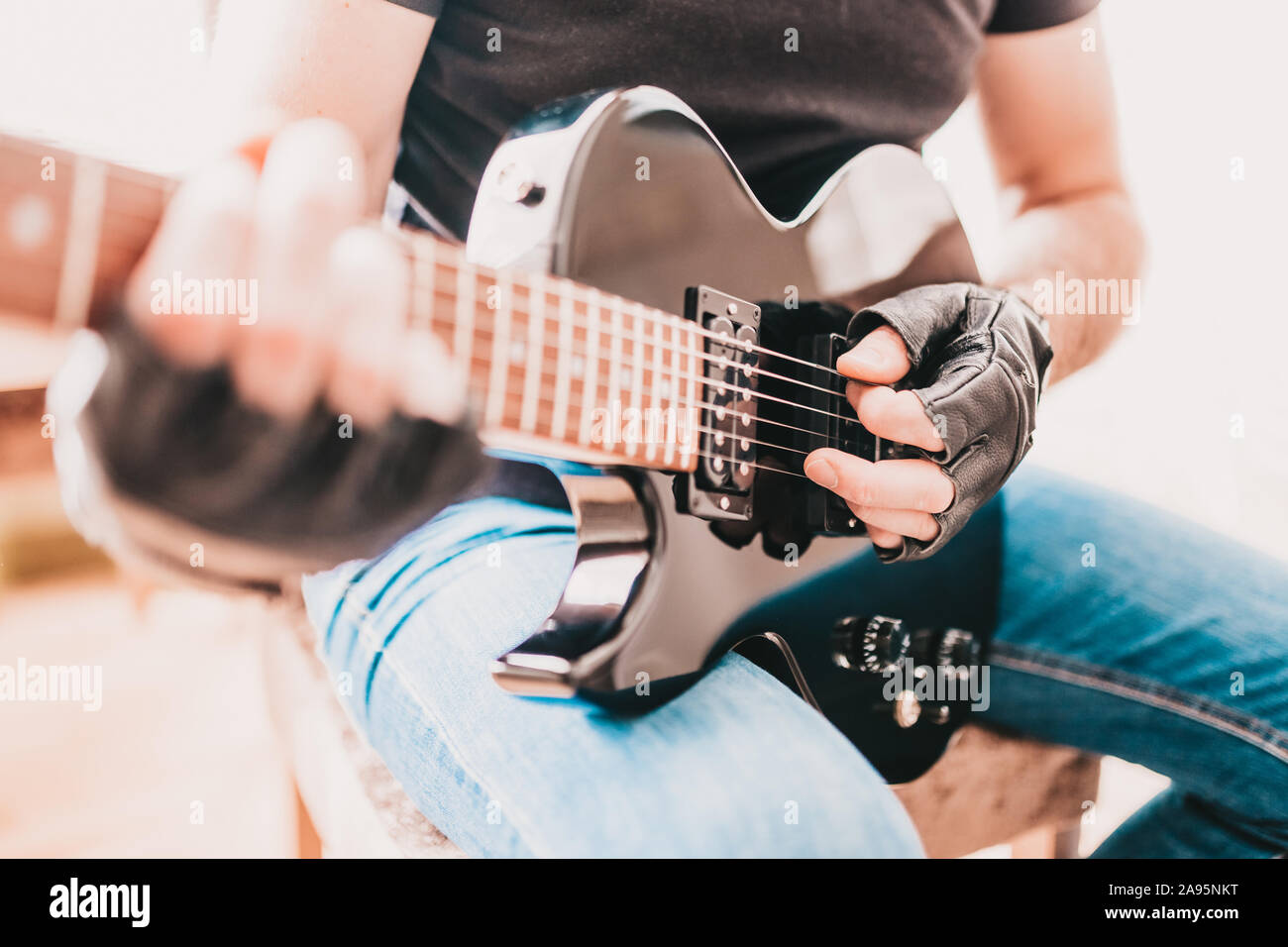 Rocker in black T-shirts and jeans playing hard rock on a left-handed black electric guitar Stock Photo