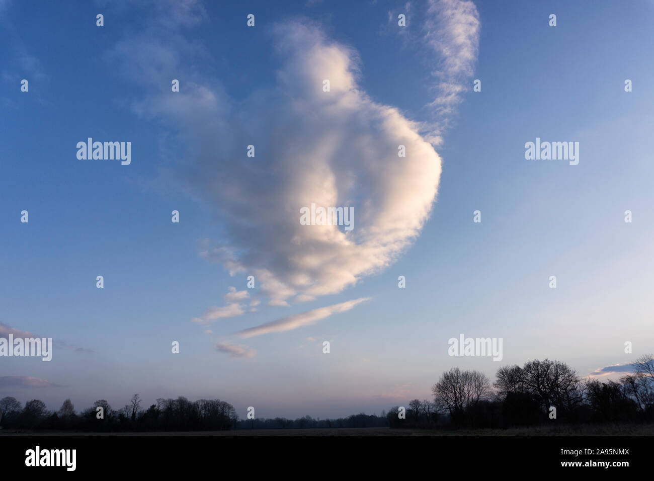 Cloud formation in the shape of a (fat) giant, genie or angel flying over fields at dusk Stock Photo