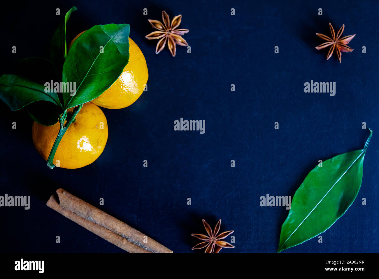 Dark textured christmas background with two tangerines, citrus leaves, star anise and cinnamon sticks. Background for banner. view from above. Stock Photo