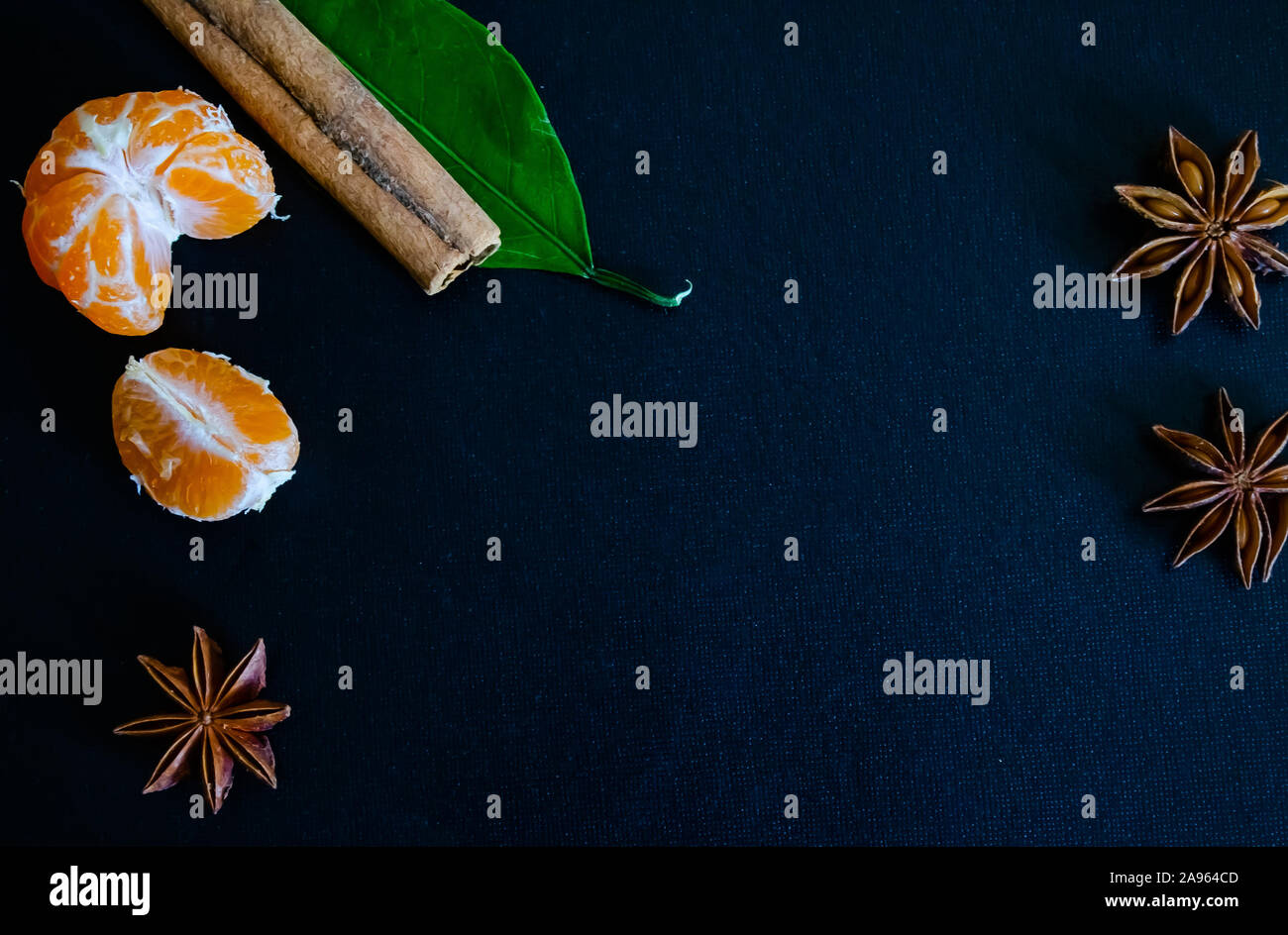 Dark textured christmas background with peeled tangerines, citrus leaves, star anise and cinnamon sticks. Background for banner, view from above. Stock Photo